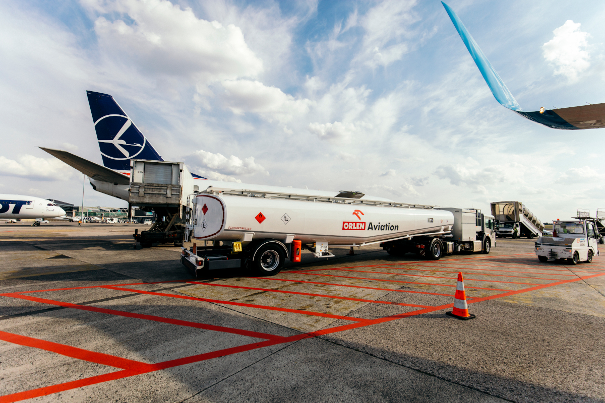 Cysterna z logo ORLEN Aviation napełniona paliwem lotniczym zaparkowana na płycie lotniska.